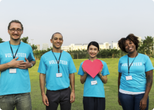 Group of diverse volunteers in blue shirts, one holding a red heart, smiling outdoors.