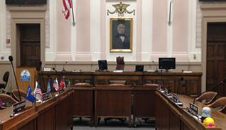 Empty government meeting room with flags, microphones, and portrait on the wall.