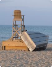 Lifeguard chair and overturned boat on a sandy beach with the ocean and sky in the background.