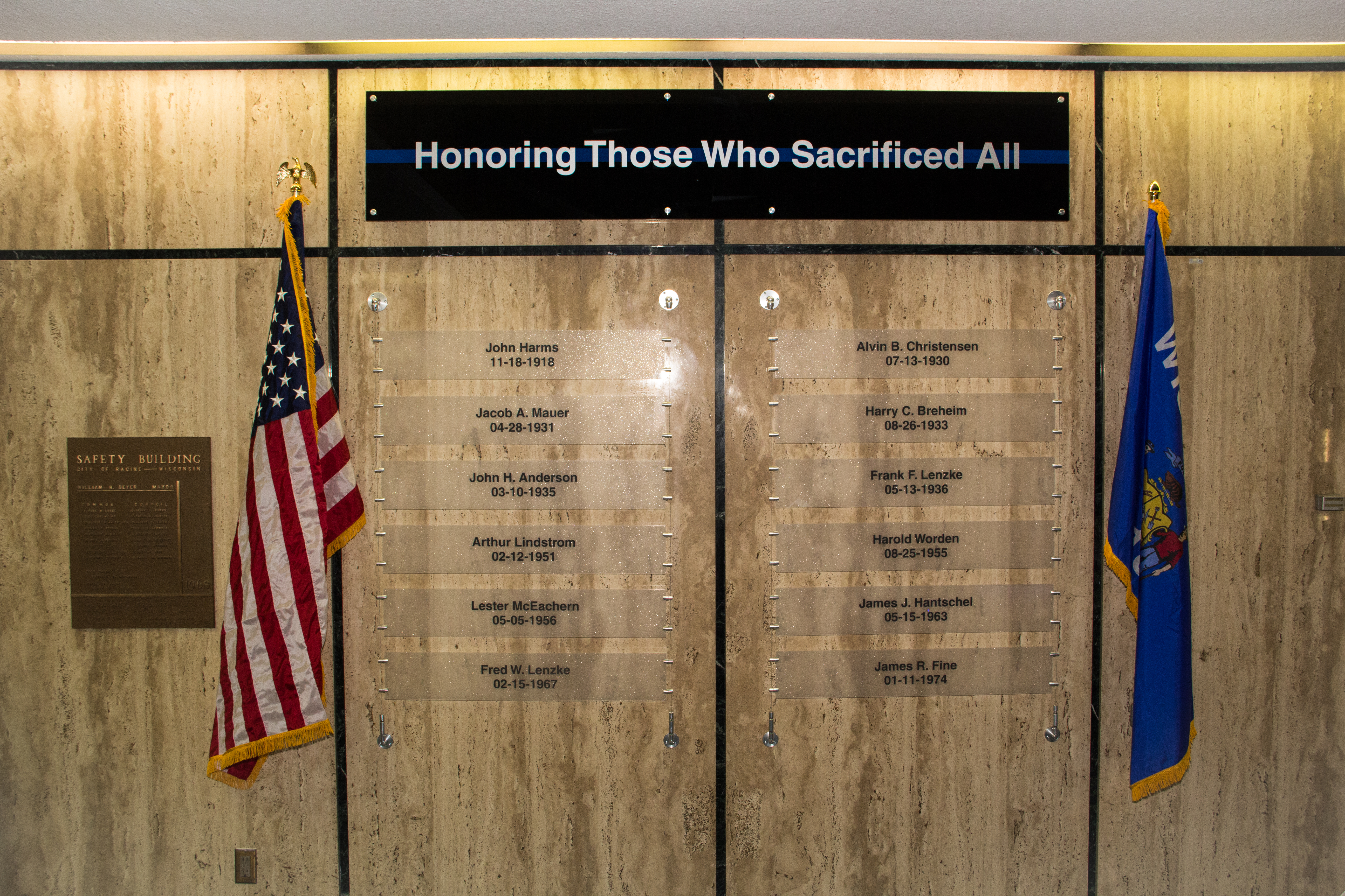 Memorial wall with names of fallen officers, American and Wisconsin flags flank the display.