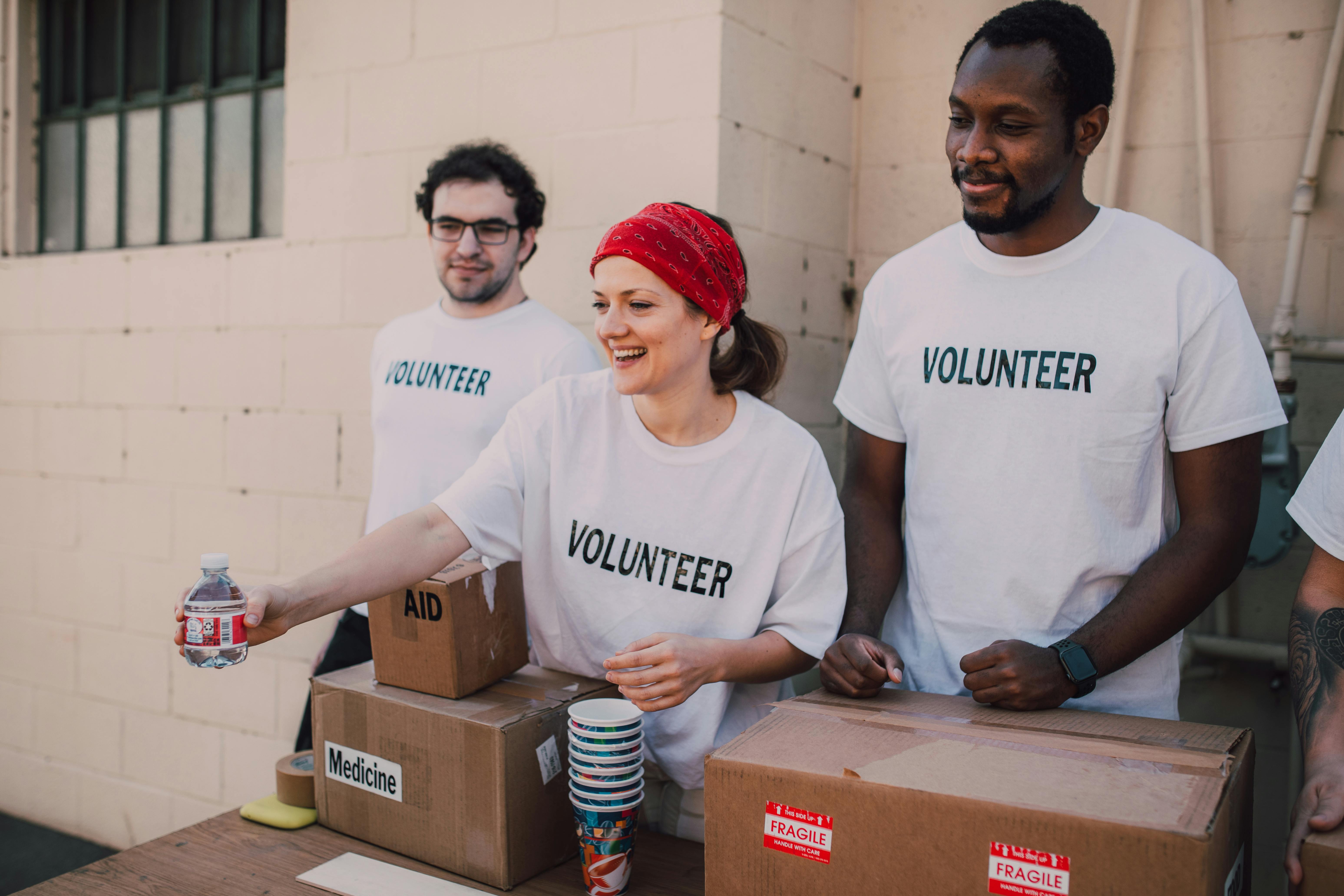 Three volunteers at a donation table with boxes of supplies and water bottles, smiling and assisting.