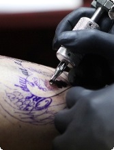 Close-up of tattoo artist tattooing a design on a person's arm, using a tattoo machine and black gloves.