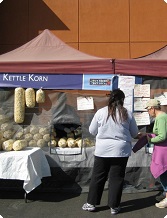 Kettle Korn stand at an outdoor market with a customer making a purchase. Bags of kettle corn are displayed.