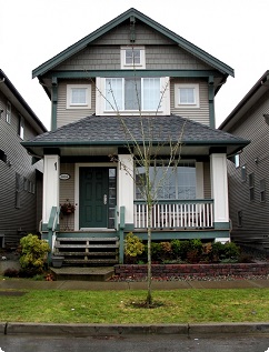Two-story house with green trim, front porch, and small tree in the yard.