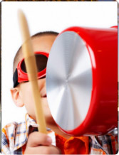 Young child with sunglasses playing a red pot like a drum with a wooden spoon, blurred motion.