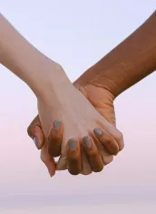 Two hands, different skin tones, clasped together against a soft, blurred background.