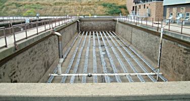 Wastewater treatment plant aeration basin with metal grating and pipes for aeration process.