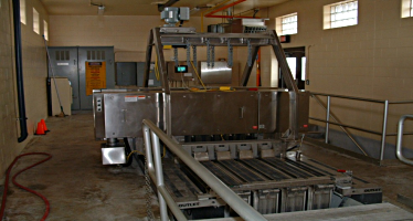 Automated bar screen system in a wastewater treatment plant, with metal railings and control panel visible.
