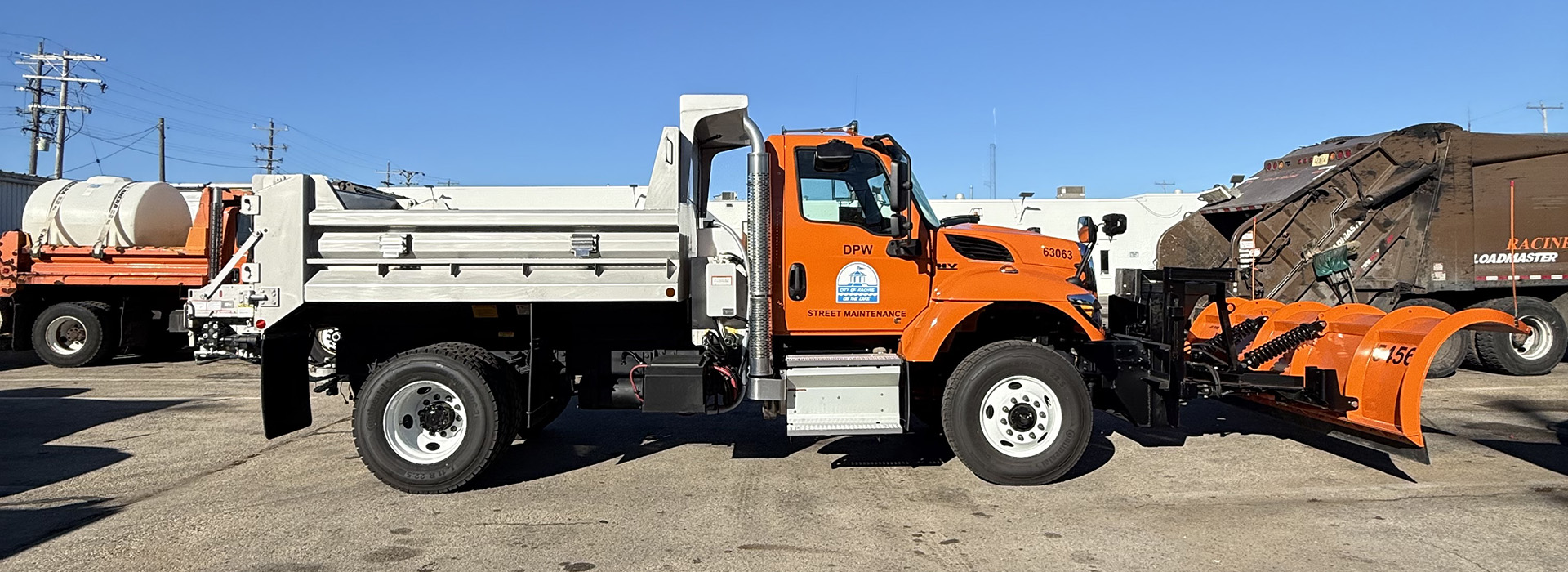 Orange snow plow truck with a white bed and plow attached to the front, parked on a concrete surface.