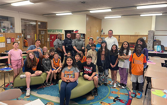 Group of elementary students with police officers and a teacher in a classroom setting.