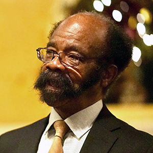 Portrait of a Black man with glasses, beard, and mustache, wearing a suit and tie, looking to the side.