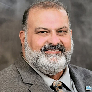 Headshot of a smiling man with a gray beard wearing a suit and tie.