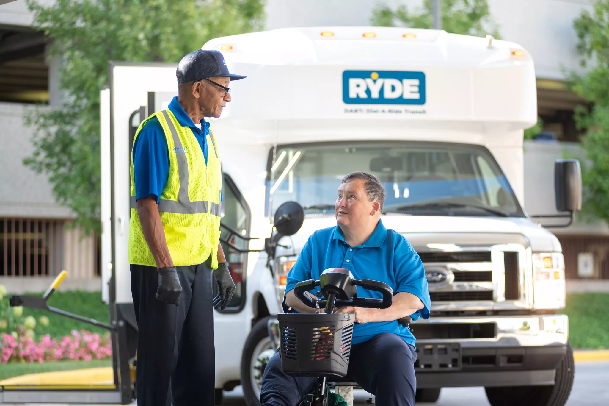 Ryde driver assisting a passenger in a mobility scooter in front of a Ryde accessible vehicle.