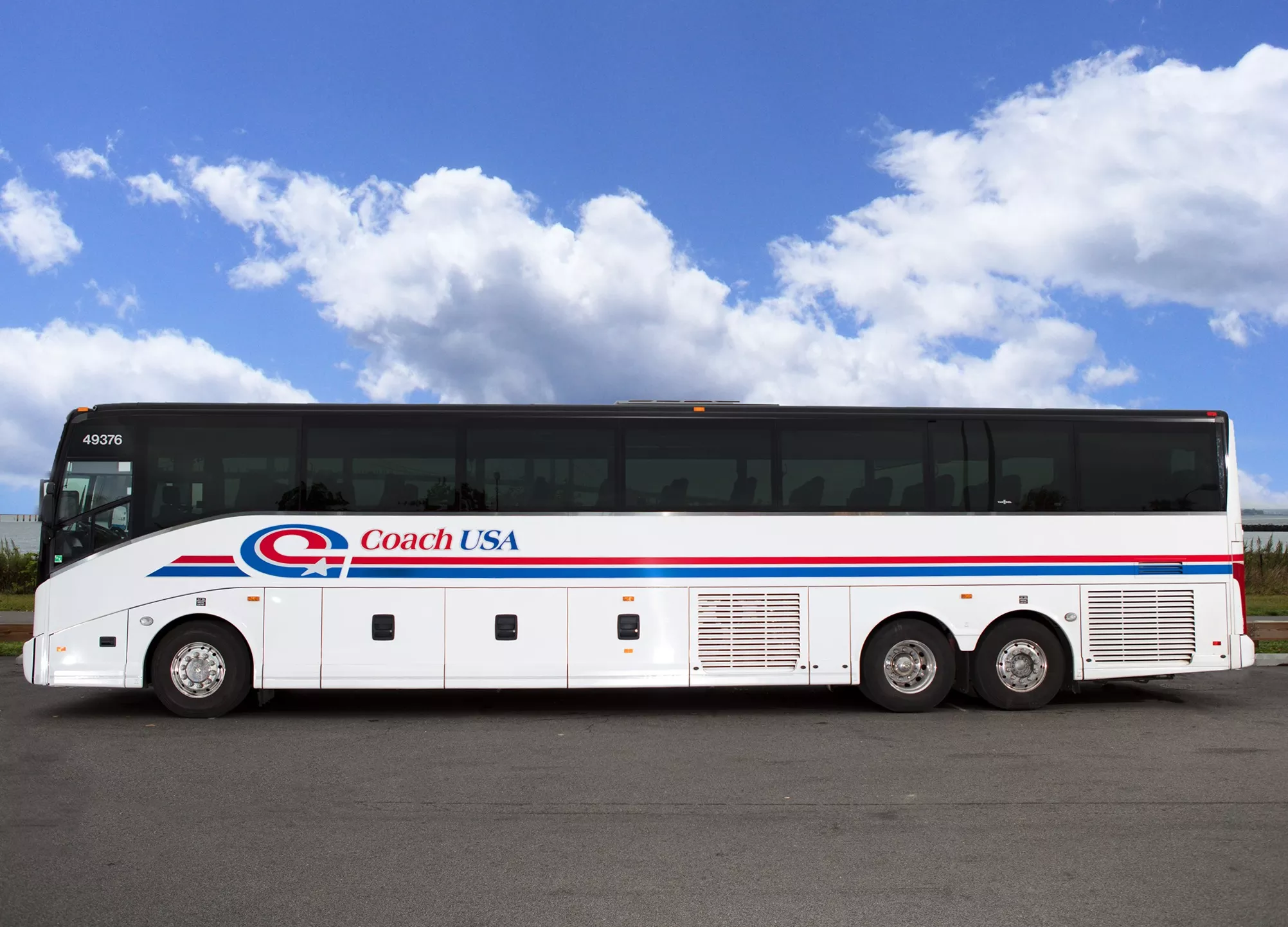 White Coach USA bus with logo and red and blue stripes against a blue sky with clouds.