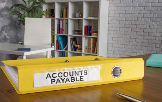 Yellow Accounts Payable binder on a desk in an office setting. Shows financial record keeping.