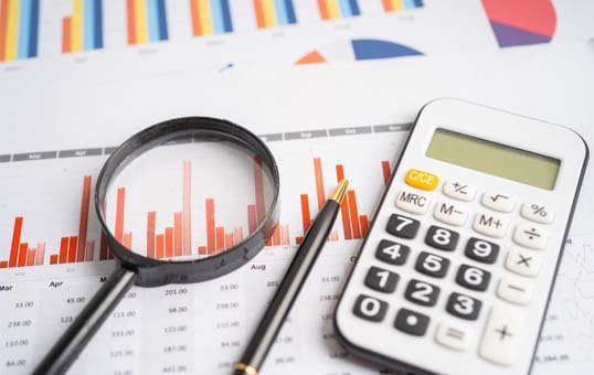 Financial analysis tools: calculator, pen, and magnifying glass on charts and graphs.