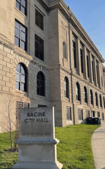 Exterior view of Racine City Hall with a sign in front. The building is made of light stone.