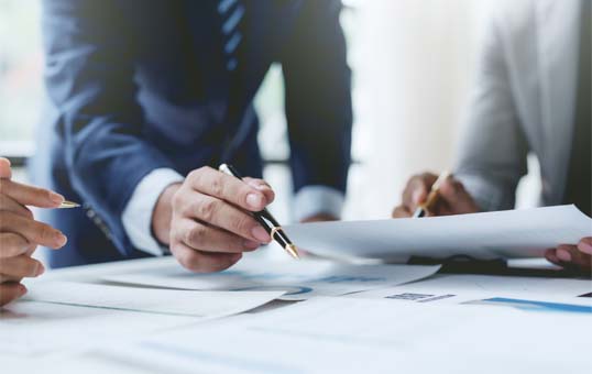 Business professionals reviewing documents at a table, one pointing with a pen, suggesting collaboration and analysis.