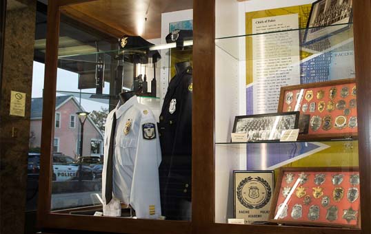Police uniform, hat, badges, and historical photos displayed in a wooden glass case.