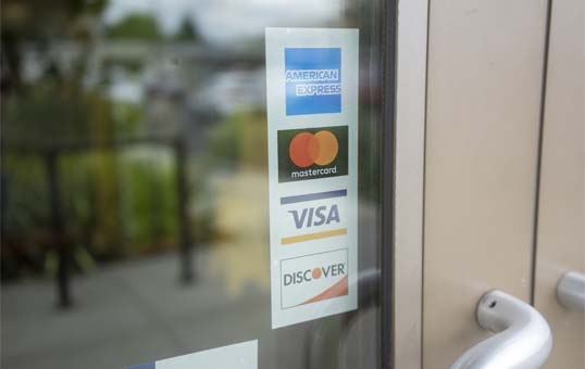 Credit card logos (American Express, Mastercard, Visa, Discover) displayed on a glass door indicating payment acceptance.
