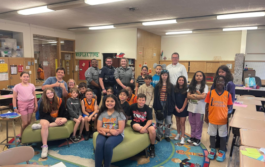 Group of students and police officers pose together in a classroom. They are smiling at the camera.