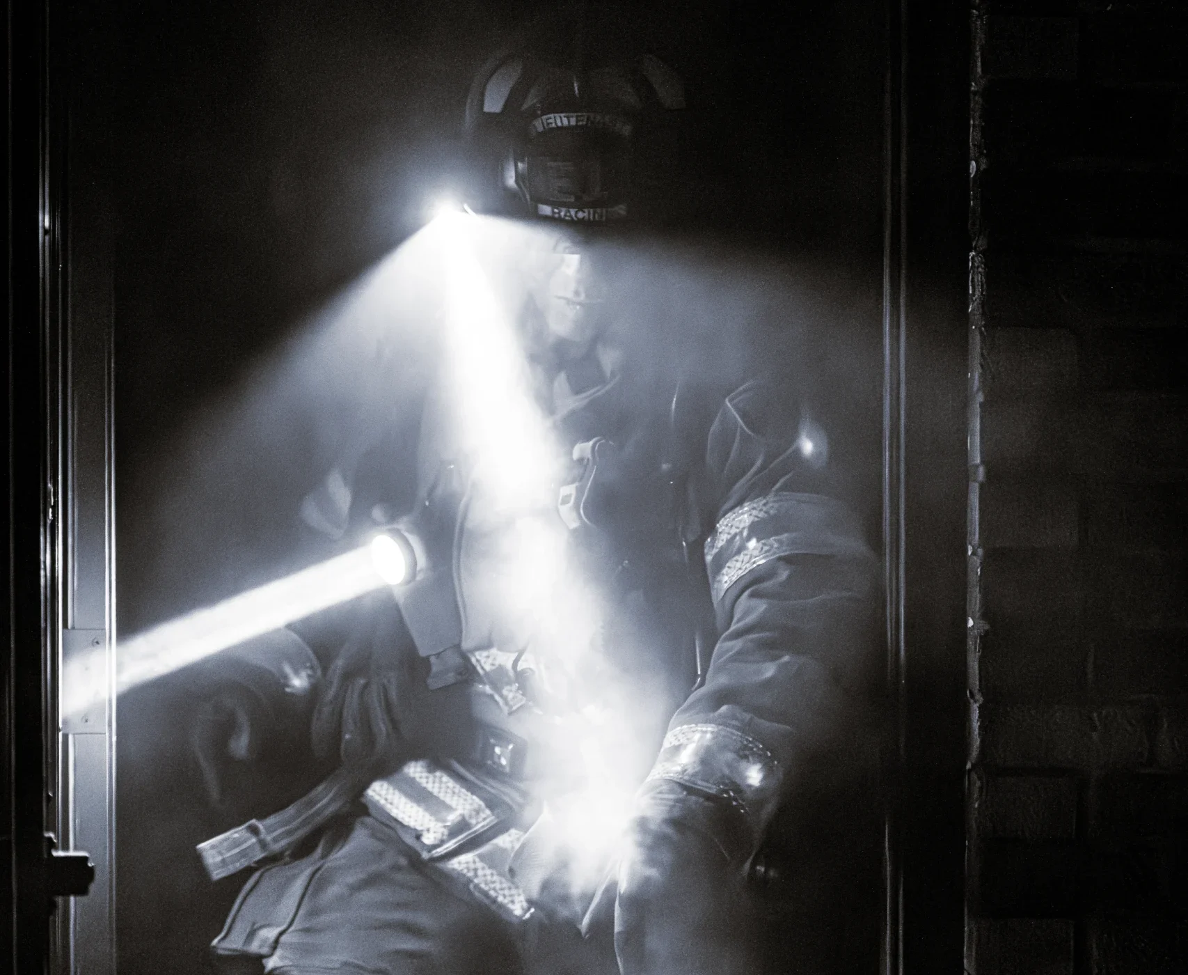 Firefighter in full gear with helmet light shining through smoke-filled doorway. Emergency response scene.