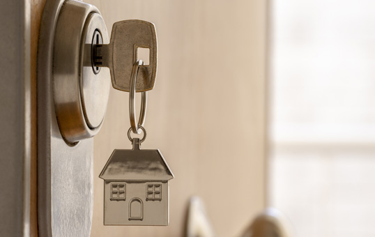 Key in a door lock with a house-shaped keychain. Symbolizes home ownership, security, or real estate.