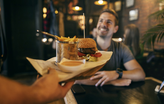 Server presenting burger and fries to smiling customer in restaurant setting.