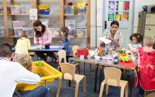 Children and teachers engaged in arts and crafts activities in a bright, organized classroom.