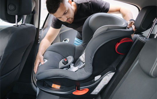Man installing a gray and black child safety seat in the back of a car, securing it for safe travel.