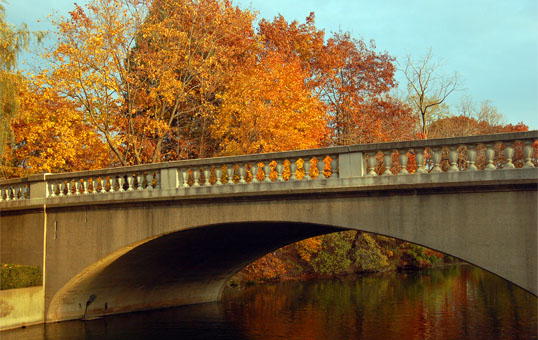 Stone bridge over water with autumn foliage in the background, featuring vibrant orange and yellow leaves.