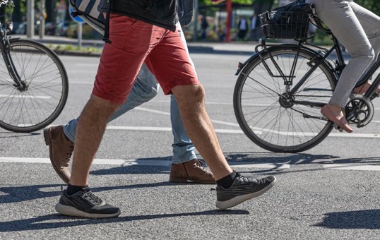 Pedestrians and cyclists share a city street, focusing on legs and wheels in motion.