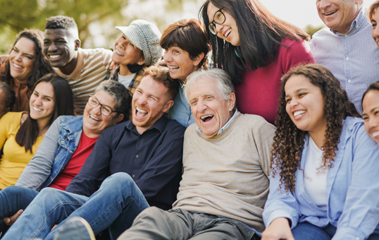 Diverse group of people smiling and laughing together outdoors, representing community and connection.
