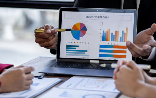Business meeting with laptop displaying business reports, charts, and graphs. Pointing with pen.