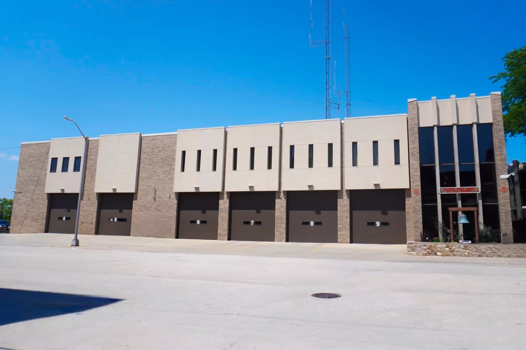 Exterior of a modern fire station with multiple garage doors and a brick and beige facade under a clear blue sky.