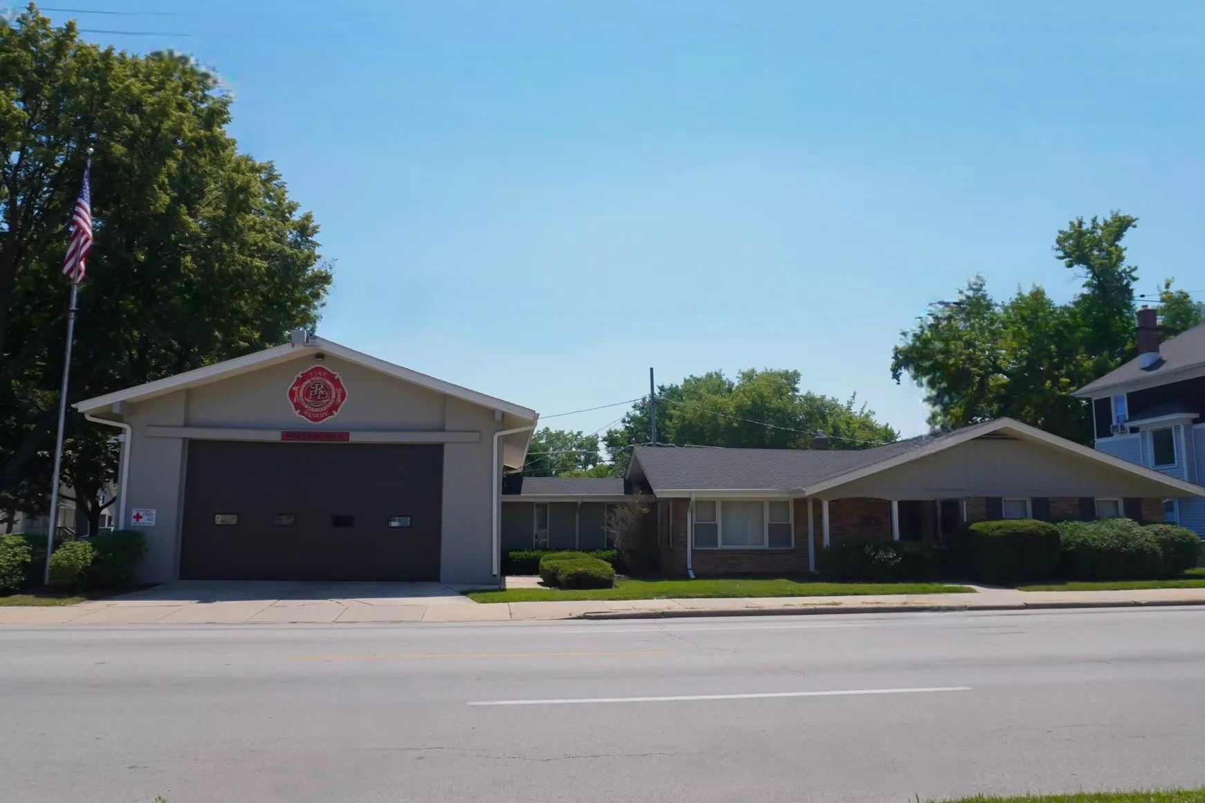 Exterior view of a fire station with a garage door and an American flag flying nearby.