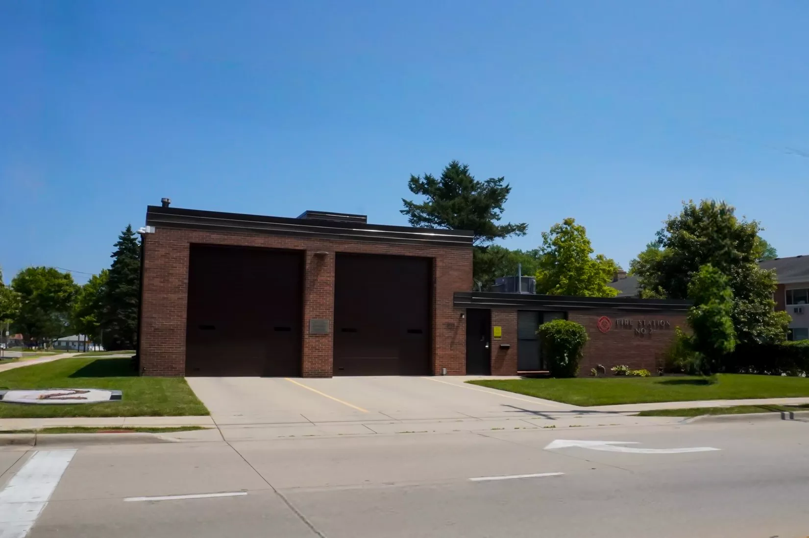 Brick fire station building with two garage doors and signage on a sunny day.
