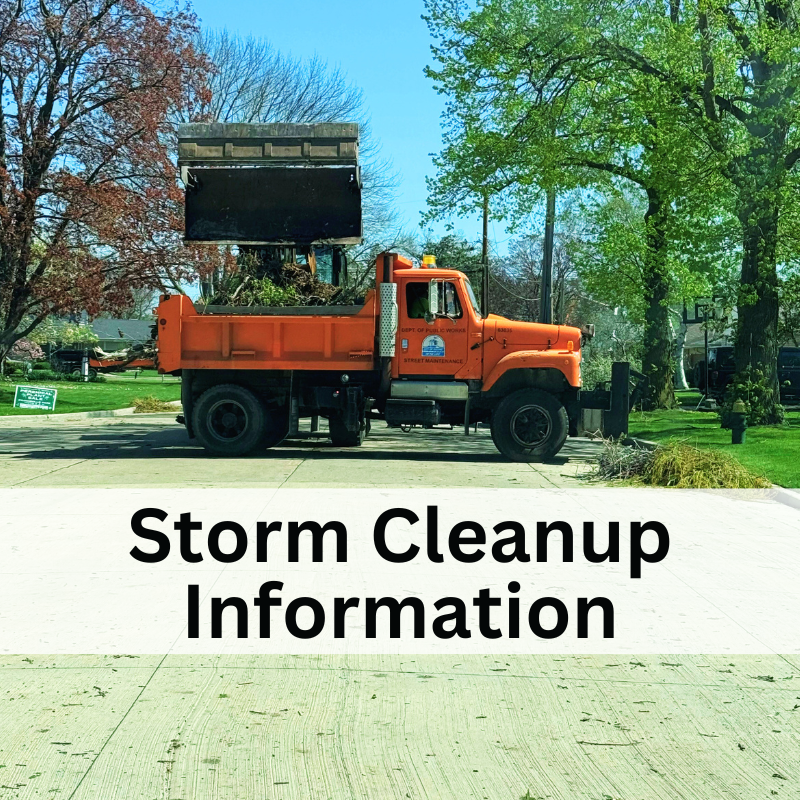 Orange dump truck filled with storm debris parked on a street, with trees and houses in the background.