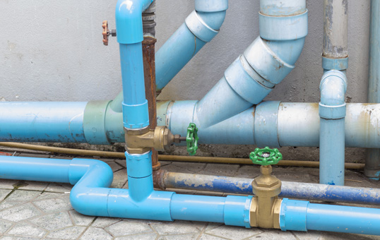 Network of blue pipes with brass valves against a concrete wall, illustrating plumbing infrastructure.