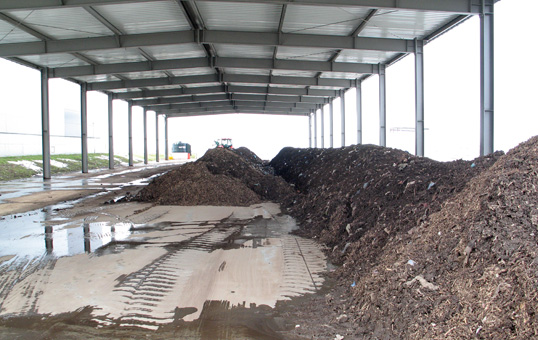 Large piles of compost under a metal roof structure, likely for storage or processing.