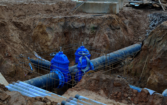 Underground pipes with blue valves in a trench, part of a water or sewage system under construction.