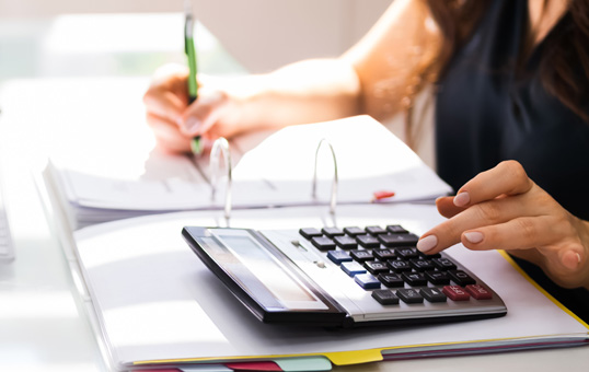 Person calculating figures with a calculator and writing in a binder. Focus on hands and calculator.