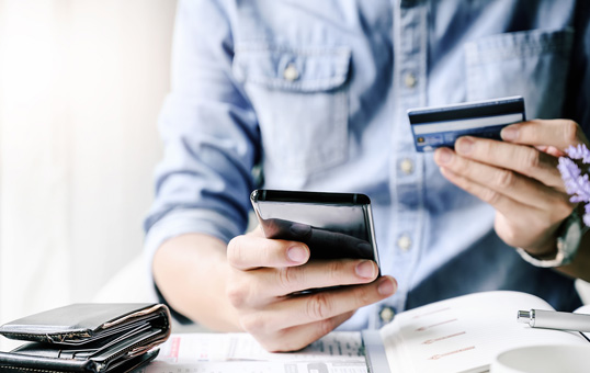 Person holding credit card and smartphone, possibly making an online payment or transaction.