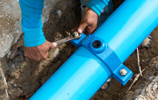 Plumber tightening bolts on a blue pipe with a wrench during installation or repair work.