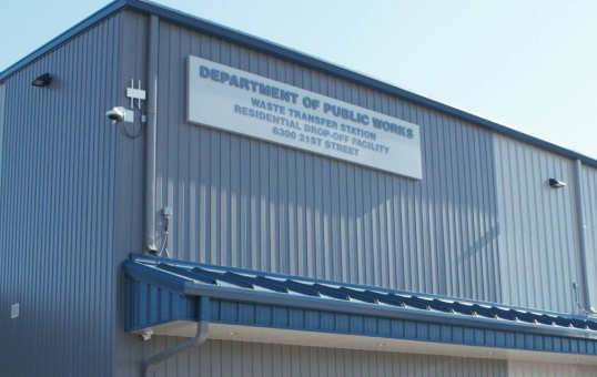 Exterior view of the Department of Public Works waste transfer station building with signage and security camera.
