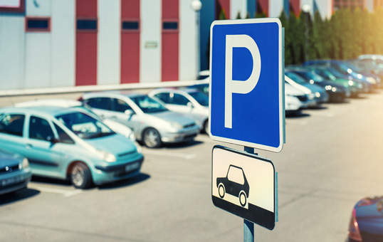 Parking sign with the letter P and a car icon, indicating designated parking area in front of a building.