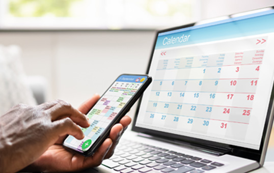 Person using a calendar app on a phone and laptop to schedule appointments.