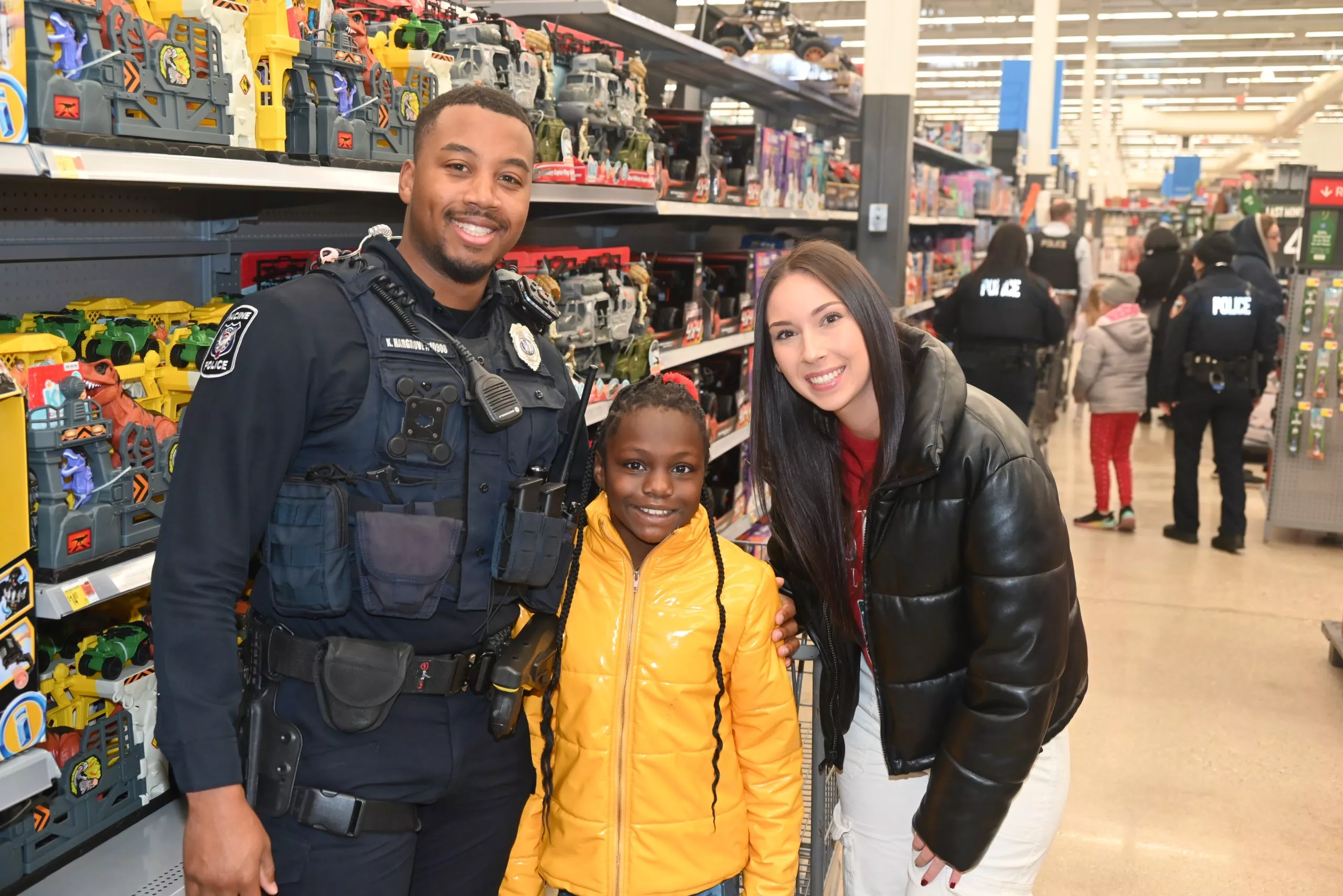 Police officer and woman pose with child in toy aisle at Walmart during a community outreach event.