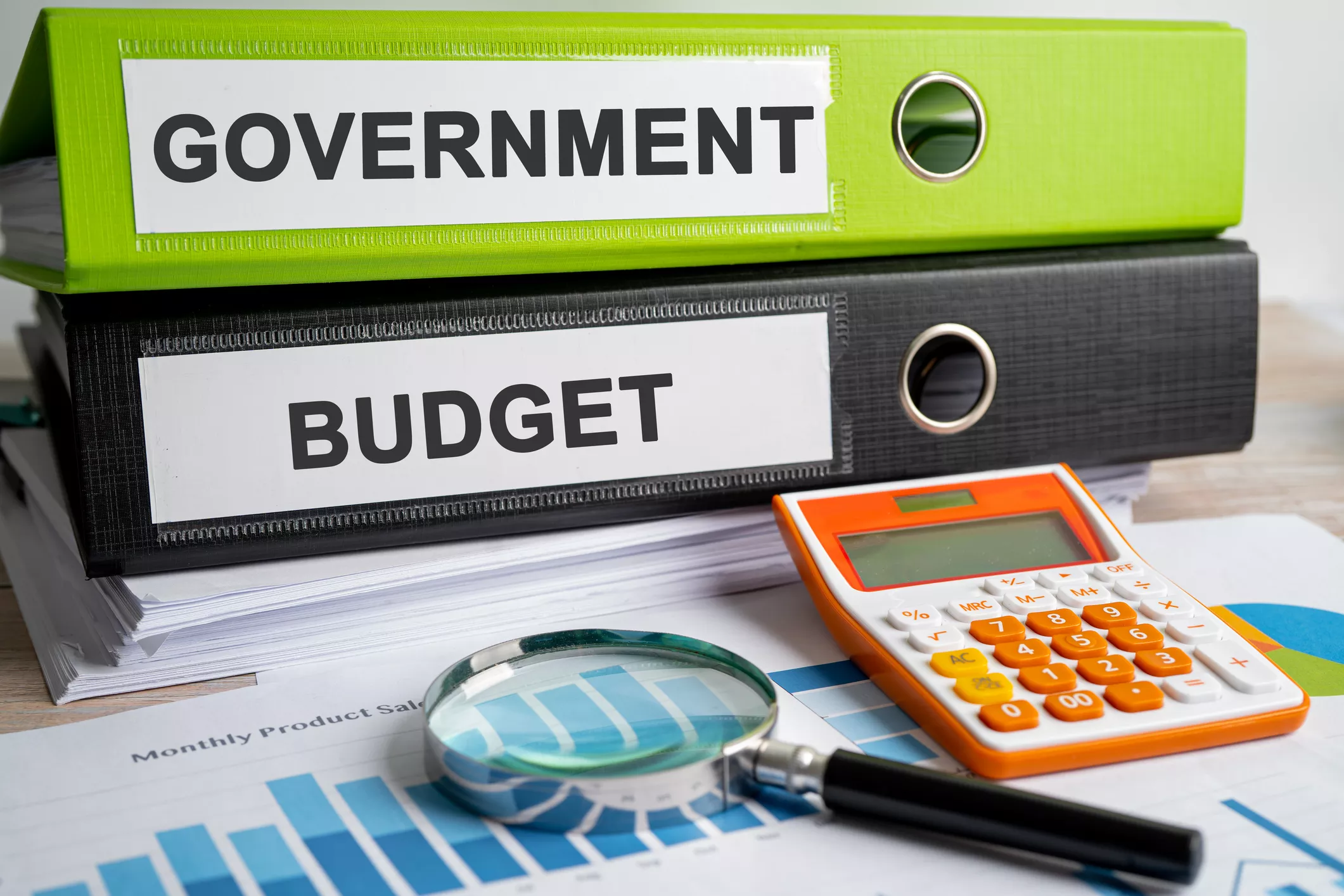 Government budget concept: binders labeled 'Government' and 'Budget' with calculator, magnifying glass, and financial charts.