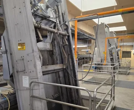 Wastewater treatment plant machinery with metal grating and railings. Pipes run overhead.